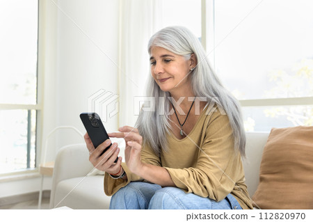 Positive grey haired old Hispanic woman typing on mobile phone 112820970