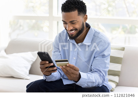 Cheerful young African customer man enjoying online shopping 112821046