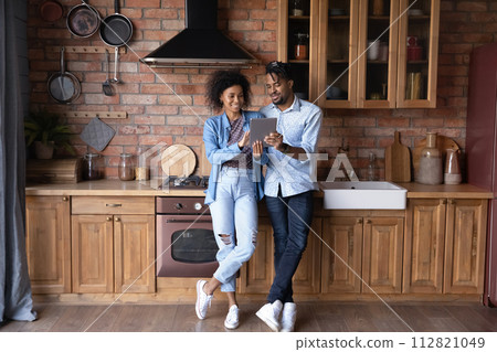African couple stand in kitchen with digital tablet discuss purchase 112821049