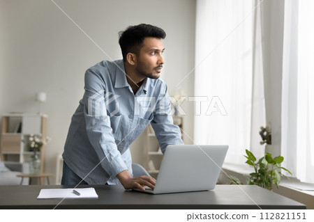 Indian man worker standing leaned at workplace desk with laptop Indian man worker standing leaned at workplace desk with laptop 112821151