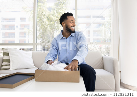 Positive young African American customer guy unpacking parcel at home Positive young African American customer guy unpacking parcel at home 112821311