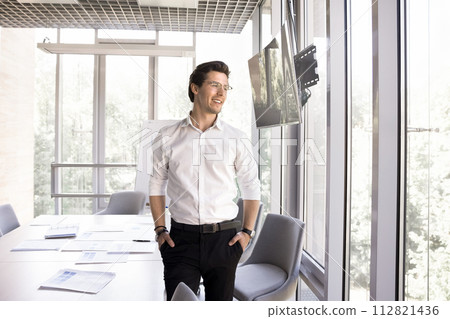 Businessman standing alone in modern conference room staring out window Businessman standing alone in modern conference room staring out window 112821436