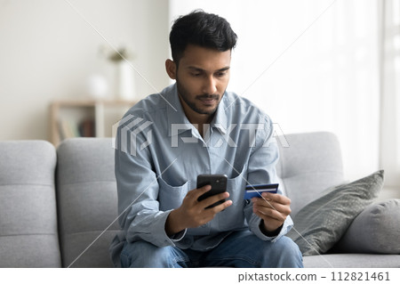Young Indian guy buying online using card and phone Young Indian guy buying online using card and phone 112821461