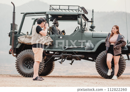 Man is focused on photographing a smiling woman who is leaning against a rugged off-road car. Man is focused on photographing a smiling woman who is leaning against a rugged off-road car. 112822260
