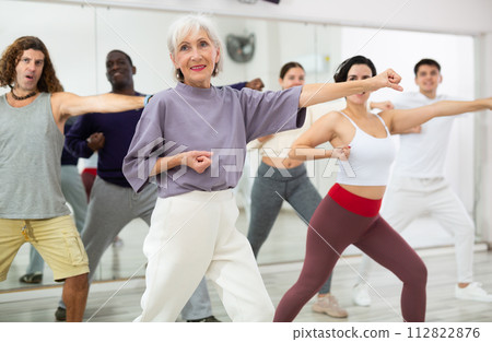 Happy mature woman practising modern dance moves with other people in dance studio Happy mature woman practising modern dance moves with other people in dance studio 112822876