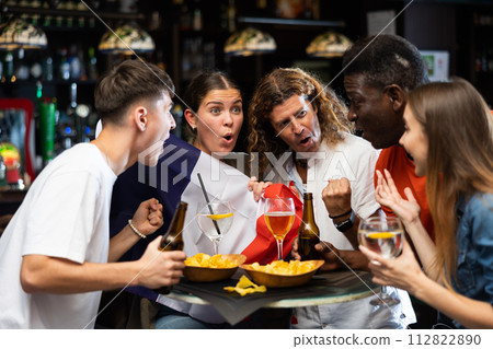 Excited diverse football supporters with flag of France watching tournament with beer and snacks in the pub Excited diverse football supporters with flag of France watching tournament with beer and snacks in the pub 112822890