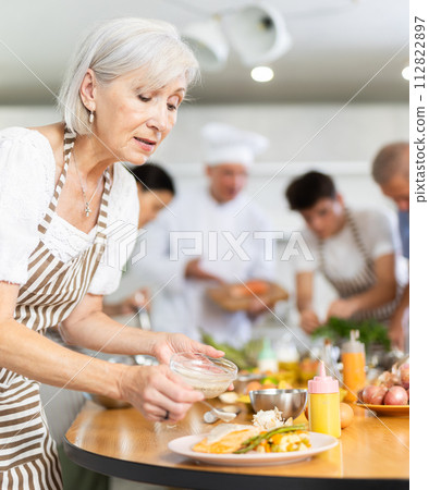 Positive old woman attendee of cooking course decorating meal made of salmon fish 112822897