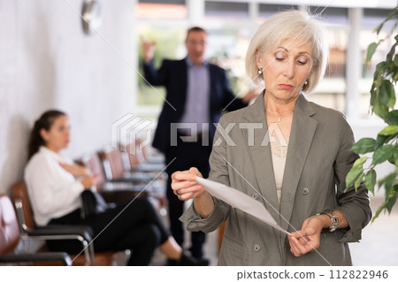 Upset old woman standing in waiting room with her back to person who is shouting at her Upset old woman standing in waiting room with her back to person who is shouting at her 112822946