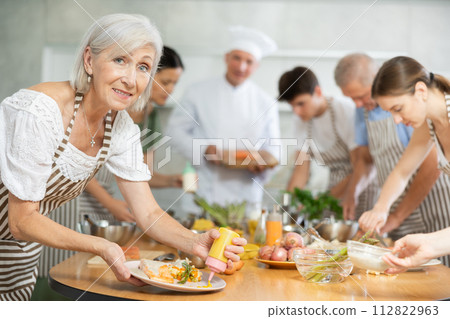 Elderly woman pouring sauce into dish at master class Elderly woman pouring sauce into dish at master class 112822963