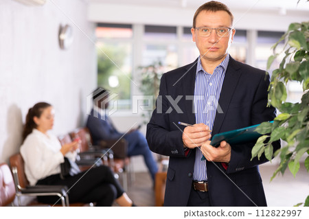 Dispassionate secretary man stands at reception with folder and list of guests and expects visitors 112822997
