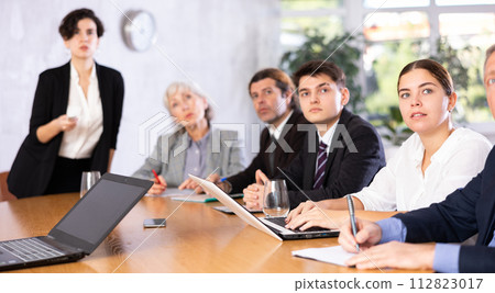Focused colleagues of different ages discussing ideas and watching presentation while Latin female turning on presentation in meeting room Focused colleagues of different ages discussing ideas and watching presentation while Latin female turning on presentation in meeting room 112823017