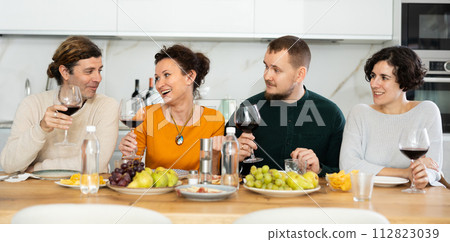 Group of joyful individuals are celebrating a holiday, enjoying drinks and conversation around table in their home Group of joyful individuals are celebrating a holiday, enjoying drinks and conversation around table in their home 112823039