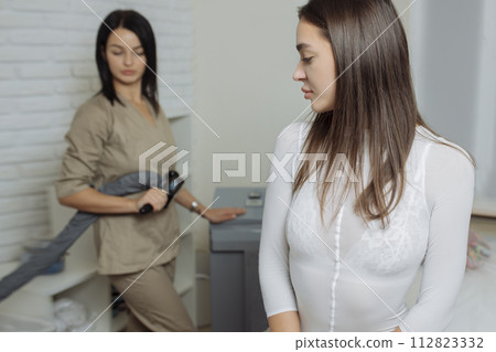 Young brunette woman in white slimming bodysuit waiting for LPG massage session. 112823332