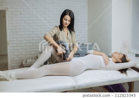 Woman in special white suit getting anti cellulite massage in a spa salon. LPG, and body contouring treatment in clinic.Reset body weight with LPG massage 112823343