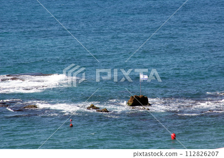 The national flag of Israel on a rock in the Mediterranean Sea in front of the city of Jaffa, Israel 112826207