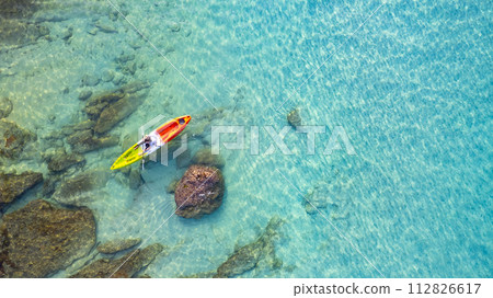 Aerial view of a woman kayaking in the blue sea and clear water. You can see corals under the sea. 112826617