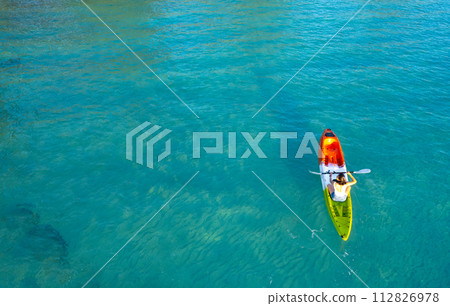 Aerial view of a woman paddle boarding in the blue sea. Clear water. You can see the coral beneath the sea. 112826978