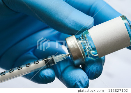 doctor's hand holds a syringe and a blue vaccine bottle at the hospital. Health and medical concepts. doctor's hand holds a syringe and a blue vaccine bottle at the hospital. Health and medical concepts. 112827102