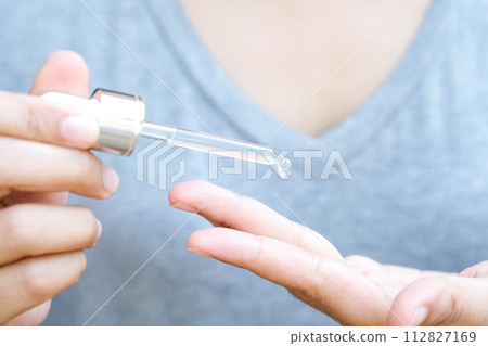 hands of a beautiful woman Dropping serum collagen moisturizer of face into clear gold bottle soft light background. Protector skin Treatment facial essence oil, Vitamin C. Beauty and spa Concept 112827169