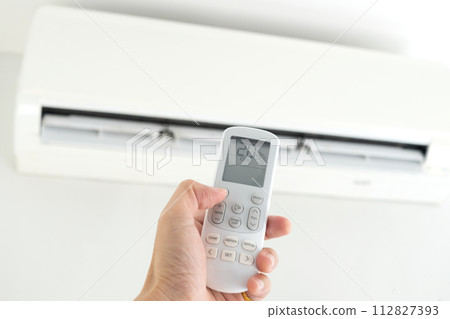 Man's hand using remote control open The air conditioner is cooled to 25 degrees Celsius in his bedroom. Health concepts and energy savings 112827393