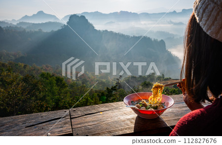 Asian female tourist eating noodles while looking at the misty mountain view 112827676