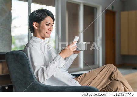 年輕的亞洲男子在家喝咖啡時看著智慧型手機 112827746