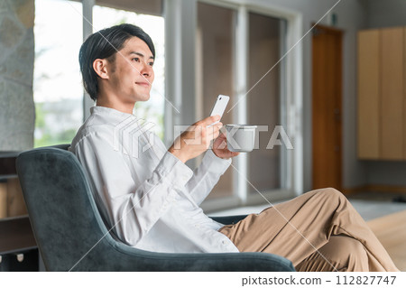 年輕的亞洲男子在家喝咖啡時看著智慧型手機 112827747