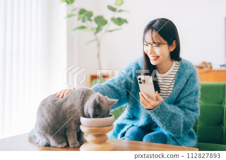 A woman petting a cat eating food 112827893