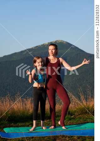 Pretty mother meditating with her daughter. Outdoor meditation in mountains. Two female doing yoga at sunrise. Pretty mother meditating with her daughter. Outdoor meditation in mountains. Two female doing yoga at sunrise. 112828332