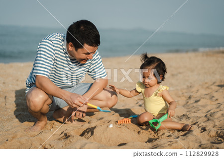 happy toddler baby girl playing sand toy with father on the sea beach happy toddler baby girl playing sand toy with father on the sea beach 112829928