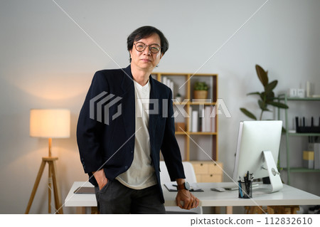 Portrait of confident middle age male entrepreneur standing at desk and looking at camera 112832610