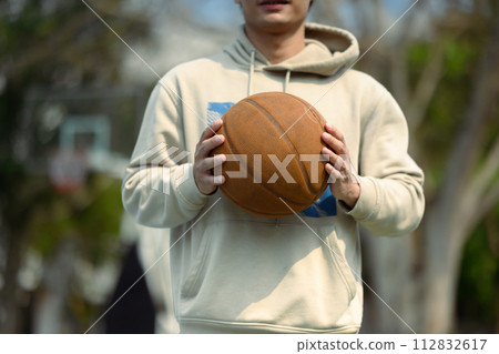 Young man holding basketball ball on an urban basketball court. People, sport and leisure lifestyle concept Young man holding basketball ball on an urban basketball court. People, sport and leisure lifestyle concept 112832617
