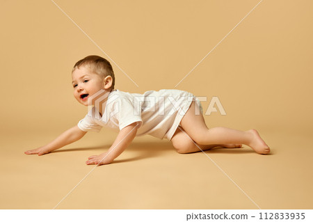 Happy, smiling little baby boy, child in t-shirt and diaper crawling, playing isolated over beige studio background Happy, smiling little baby boy, child in t-shirt and diaper crawling, playing isolated over beige studio background 112833935