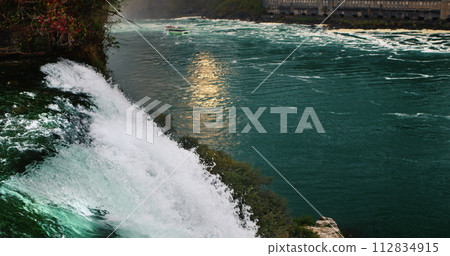 Evening at Niagara Falls. The river reflects the setting sun, in the foreground a powerful stream of water. Slow motion 120 fps video 112834915