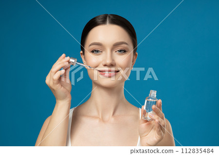 A brunette applies cosmetics with a dropper to her face A brunette applies cosmetics with a dropper to her face 112835484