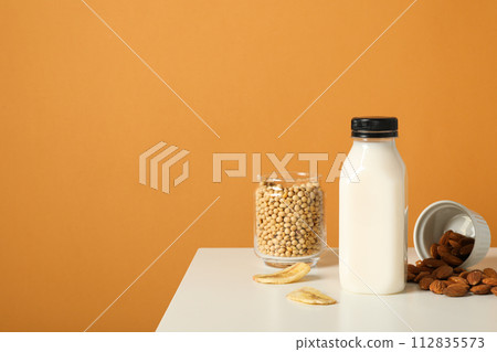 Bottle of alternative milk, nuts and soybeans on orange background, space for text Bottle of alternative milk, nuts and soybeans on orange background, space for text 112835573