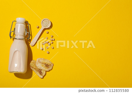 Bottle of alternative milk, soybeans and sliced bananas on yellow background, space for text Bottle of alternative milk, soybeans and sliced bananas on yellow background, space for text 112835580