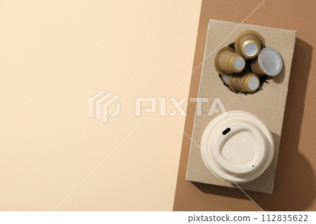 Coffee capsules and paper cup in paper stand on brown and beige background, space for text 112835622