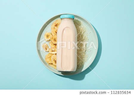Bottle with milk on plate with rice and sliced bananas on blue background, top view Bottle with milk on plate with rice and sliced bananas on blue background, top view 112835634