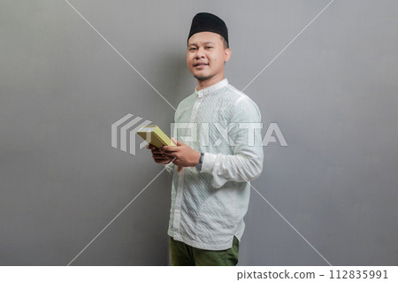 Asian Muslim man holding prayer beads and reading Qur'an Asian Muslim man holding prayer beads and reading Qur'an 112835991