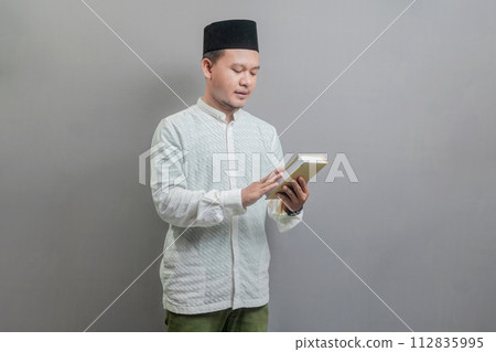 Asian Muslim man holding prayer beads and reading Qur'an Asian Muslim man holding prayer beads and reading Qur'an 112835995