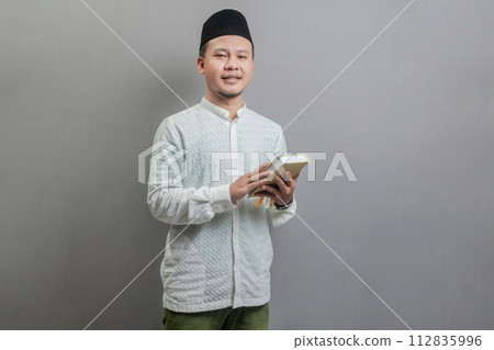 Asian Muslim man holding prayer beads and reading Qur'an Asian Muslim man holding prayer beads and reading Qur'an 112835996