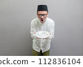Happy asian muslim man holding empty white plate or dish 112836104