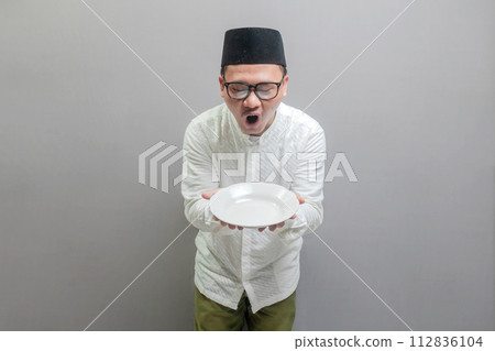 Happy asian muslim man holding empty white plate or dish 112836104