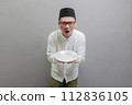 Happy asian muslim man holding empty white plate or dish 112836105