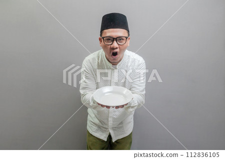 Happy asian muslim man holding empty white plate or dish 112836105