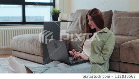 Redhead woman is working on laptop computer in the living room at home. Modern technology, internet, online shopping and people concept. Redhead woman is working on laptop computer in the living room at home. Modern technology, internet, online shopping and people concept. 112836562