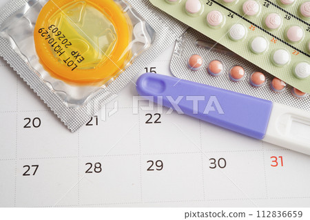 Pregnancy test with birth control pills and condom for female on calendar, ovulation day. Pregnancy test with birth control pills and condom for female on calendar, ovulation day. 112836659