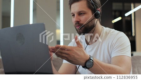 Young man sitting at home wear wireless headset having video conference. Concept of remote work or education. 112836955