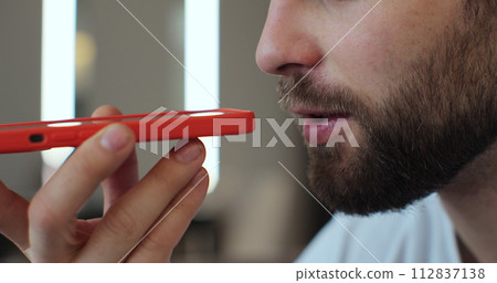 Close-up of bearded man recording answering by audio message in social network on mobile phone. Man call on phone closeup, use loudspeaker at home. 112837138